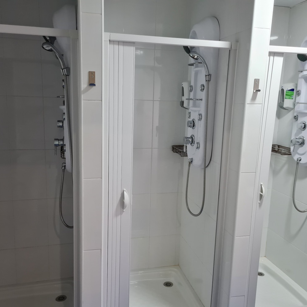 Three white tiled shower stalls. One with a closed accordion door, two with shower heads.