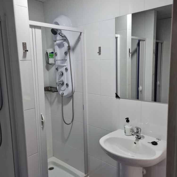 Small white bathroom with shower stall, sink, and mirror.