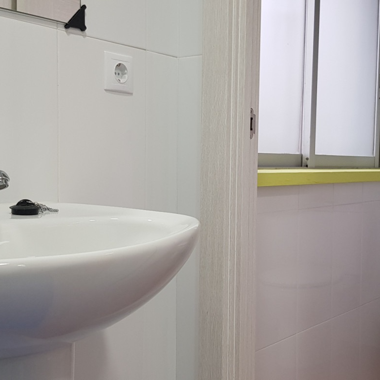 White bathroom sink, outlet on wall, doorway to window.