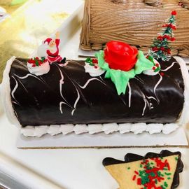 Chocolate holiday cake with red rose topper, white drizzle, and small Christmas decorations on a tray