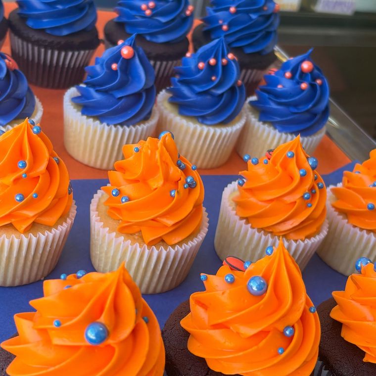 Tray of cupcakes with bright orange and blue frosting, topped with silver sprinkles