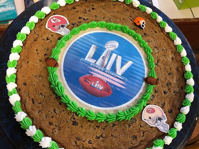 Round cookie cake with green frosting border and a blue LIV center design, decorated with small sports helmet images.