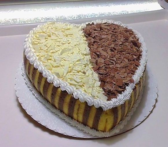 Heart-shaped cake with white and chocolate shavings on top, sitting on a cake board.