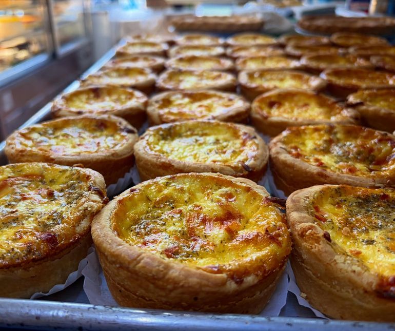 Tray of golden-brown savory tarts with browned tops in a bakery display case