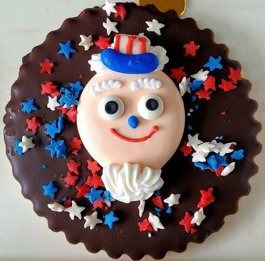 Festive round cake with a smiling clown face, chocolate icing, and red, white, and blue star sprinkles