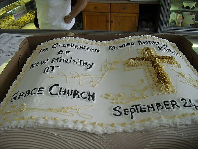 Decorated white church cake with gold cross, “Grace Church,” and “September 21” written on top.