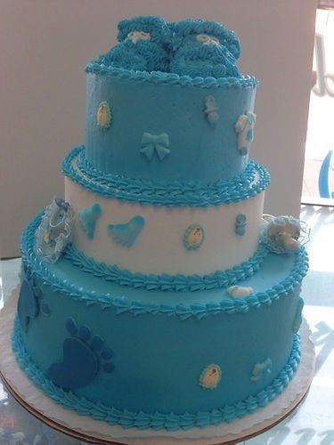 Three-tier blue and white decorated cake with bows and baby-themed accents