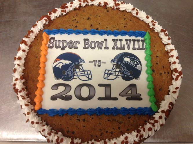 Super Bowl XLVIII 2014 cake with Seahawks and Broncos logos on white and orange frosting.