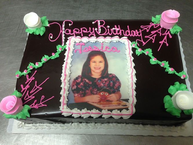 Chocolate birthday cake with pink decorations and a framed photo topper on top.