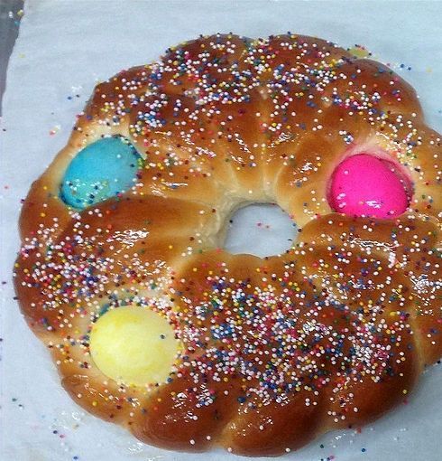 Round braided bread topped with sprinkles and three pastel candies on a white surface