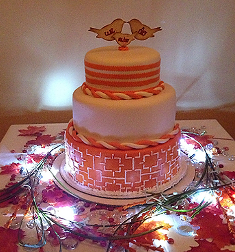 Three-tiered decorated cake with white icing and lights on a floral table runner