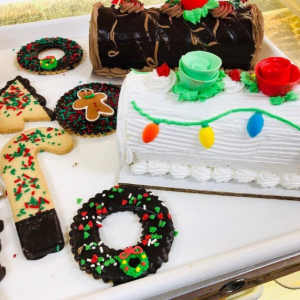 Assorted decorated holiday cakes and cookie wreaths with red, green, and white frosting on a tray