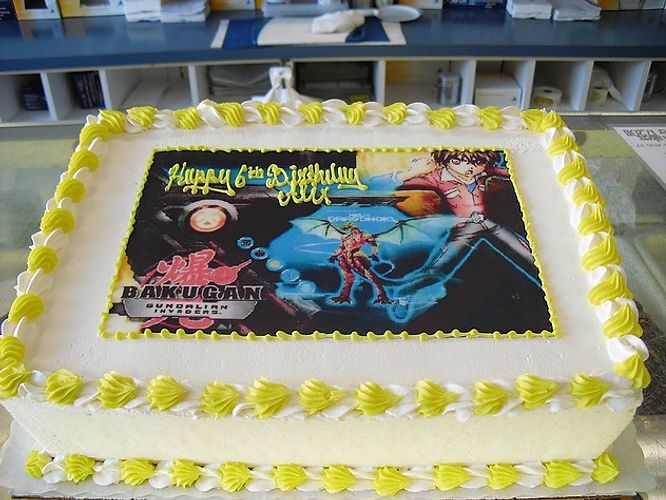 Rectangular cake with yellow frosting and a colorful printed image on top, displayed on a table
