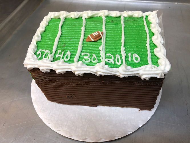 Football field cake with green frosting, white yard lines, and a small football on top
