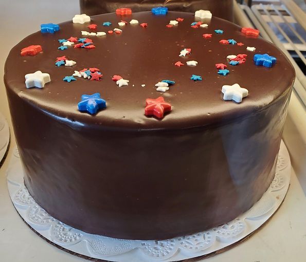 Chocolate frosted cake topped with red, blue, and white star sprinkles on a white doily-lined plate