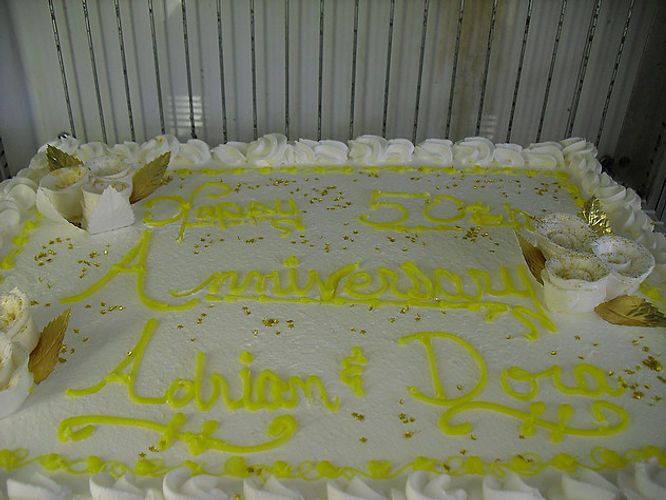 Decorated white sheet cake with yellow icing reading “50 Anniversary” and “Laion? & Doe” in a box interior