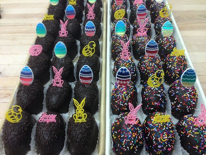 Rows of dark chocolate Easter eggs decorated with colorful icing and sprinkles on trays