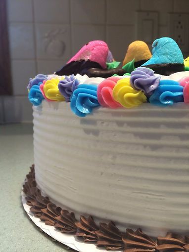 Round white cake with colorful frosting swirls and pink, yellow, and blue decorations on top