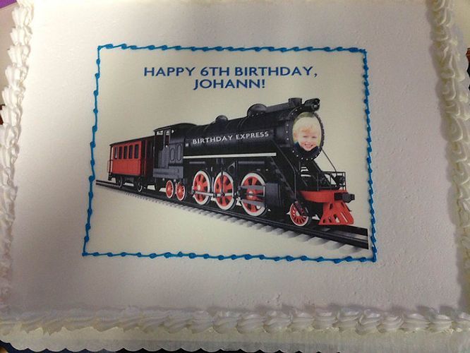 Blue-bordered birthday cake topper with a black steam train and the text “Happy 6th Birthday, Johann!”