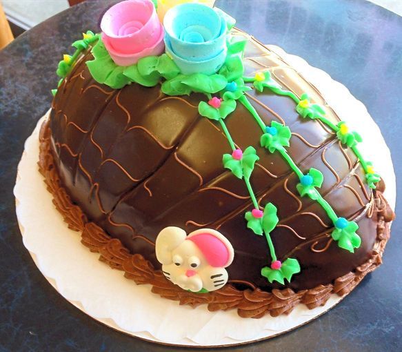 Chocolate egg cake with pink and blue cups, green vines, and a small bunny decoration on a white plate