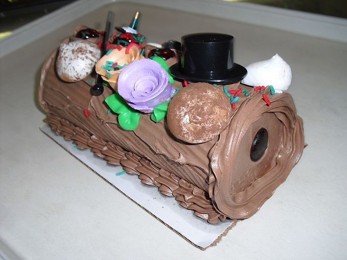 Chocolate log cake with brown frosting, purple rose, and a black top hat decoration