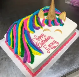 Unicorn-themed birthday cake with rainbow mane, gold horn, and “Happy Birthday Emma” icing on a white tray