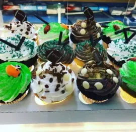 Assorted decorated cupcakes with green, white, and chocolate frosting in a bakery display case
