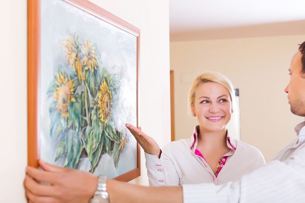 A man and a woman are hanging a painting on a wall.