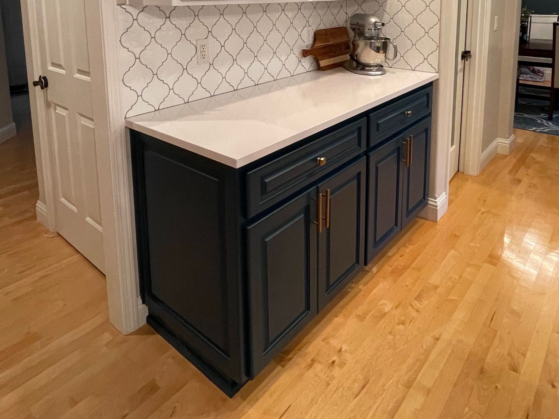 Dark blue kitchen cabinets with white countertop, brass hardware, and white tile backsplash.