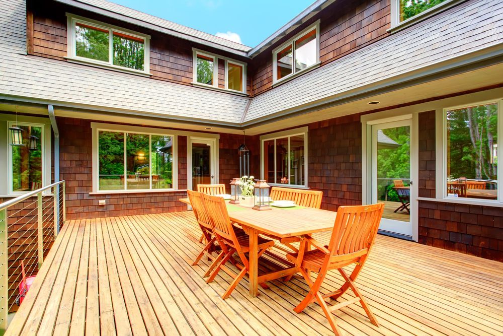 Wooden deck with table and chairs outside a brown house with many windows.