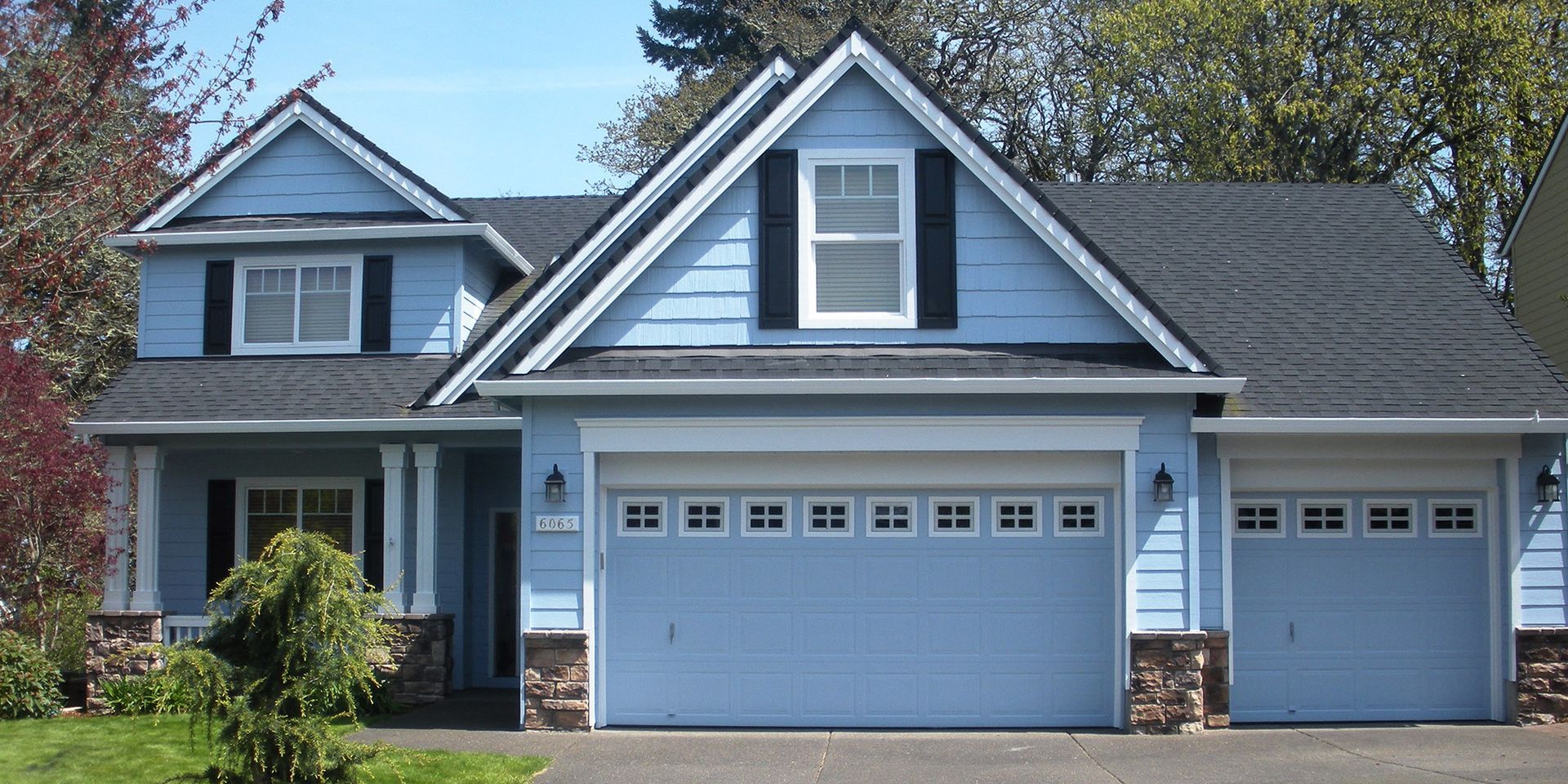 A blue house with two garage doors and a black roof