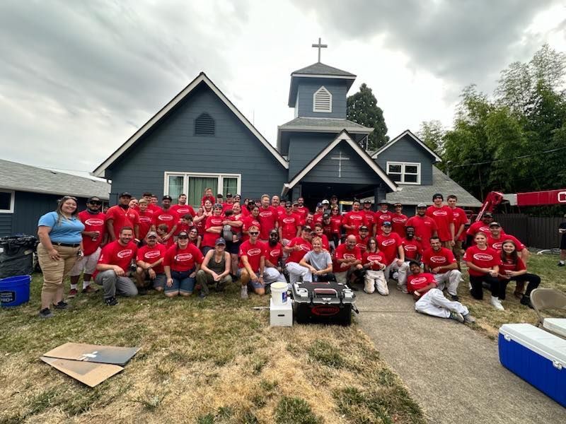 Group of people in red shirts pose in front of a blue church.