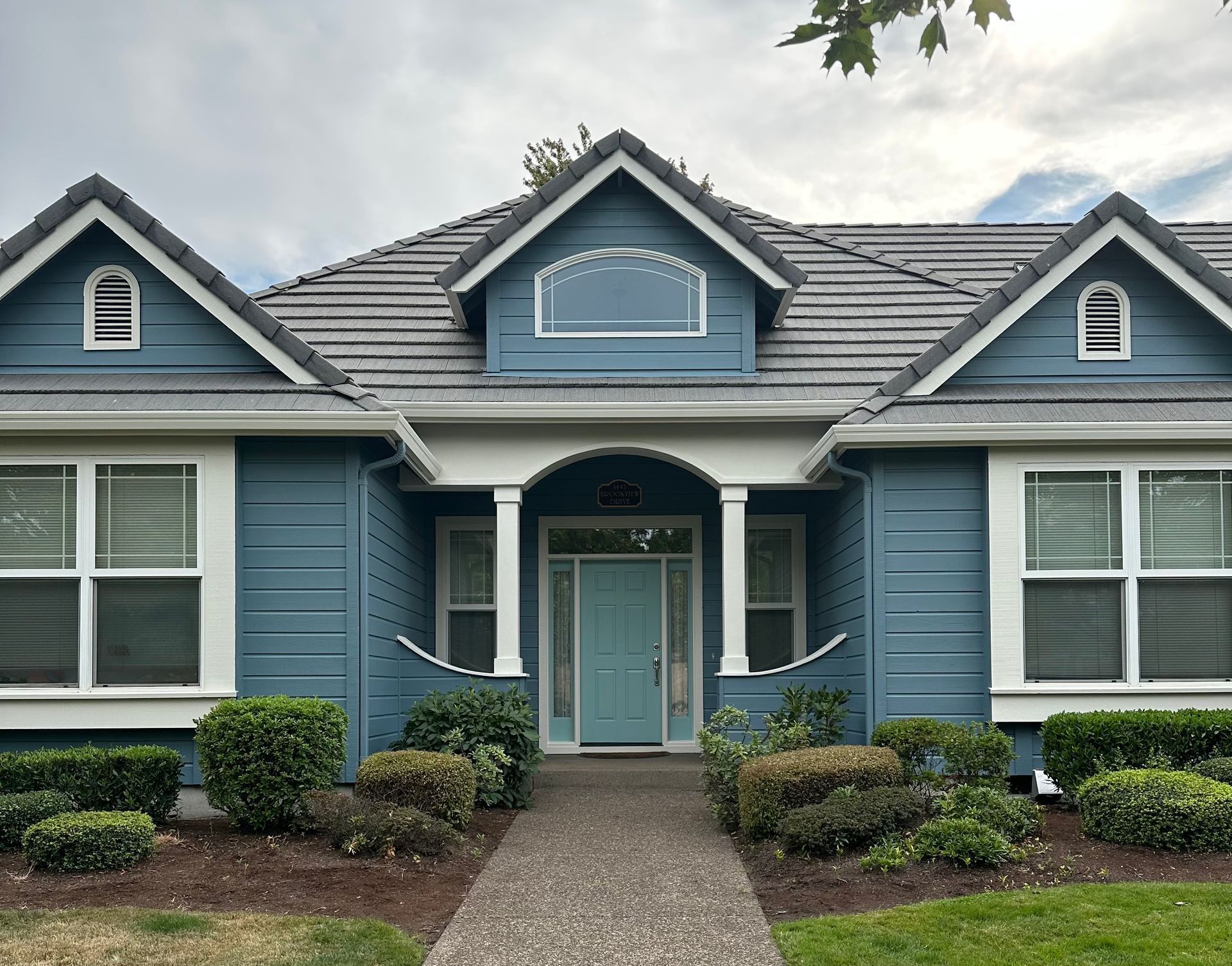 Blue house with white trim, arched entryway, and dark gray roof.