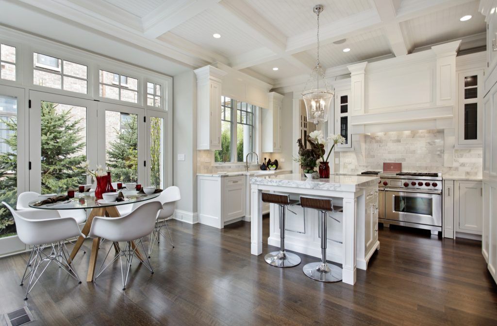 A kitchen and dining room in a house with white cabinets and hardwood floors.