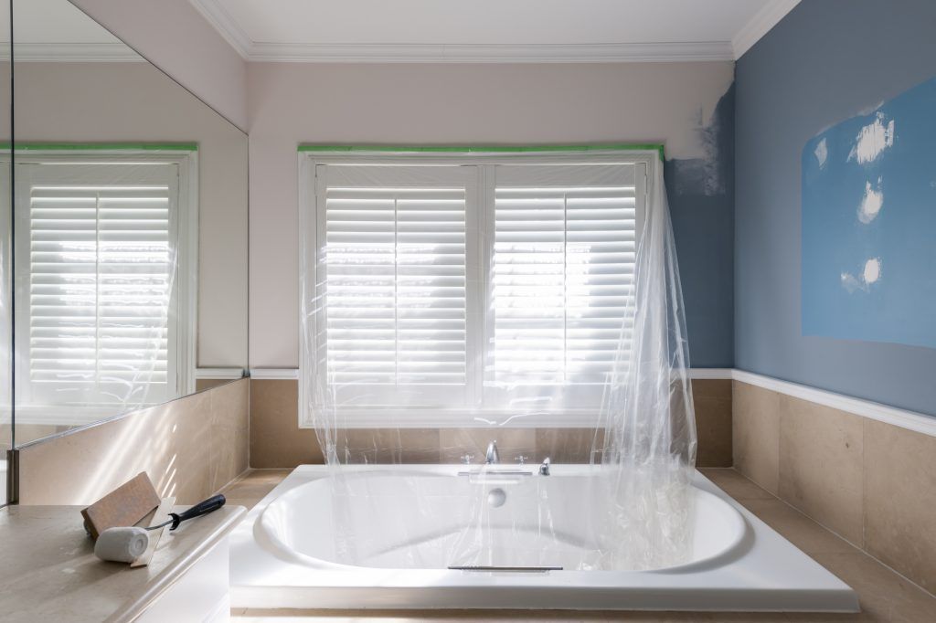 Bathroom with bathtub and window being painted. Plastic sheeting protects the tub and blinds.