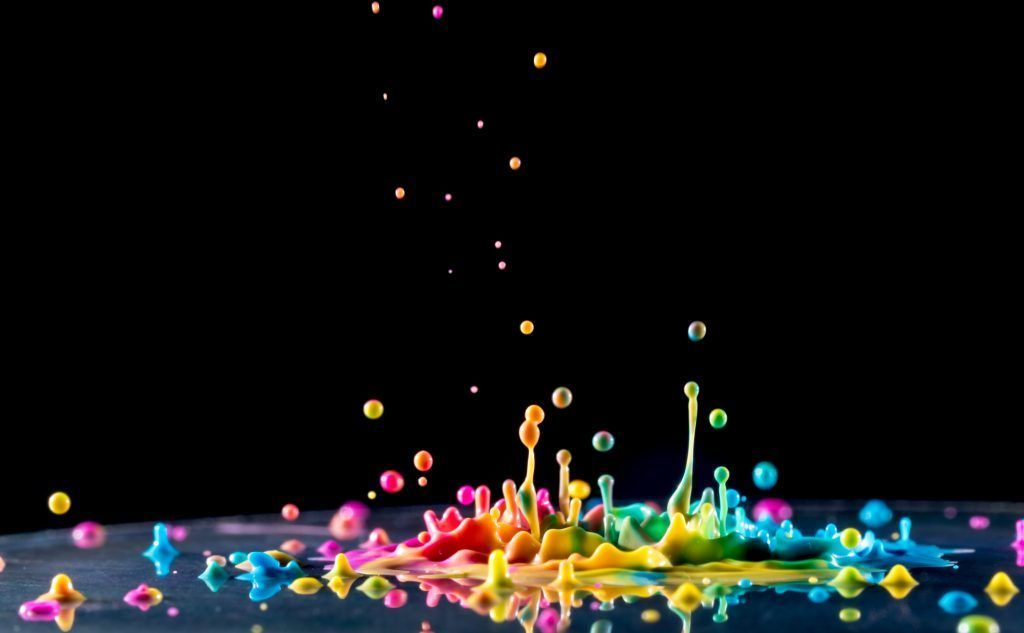 A rainbow of colors is splashing into a pool of water on a black background.
