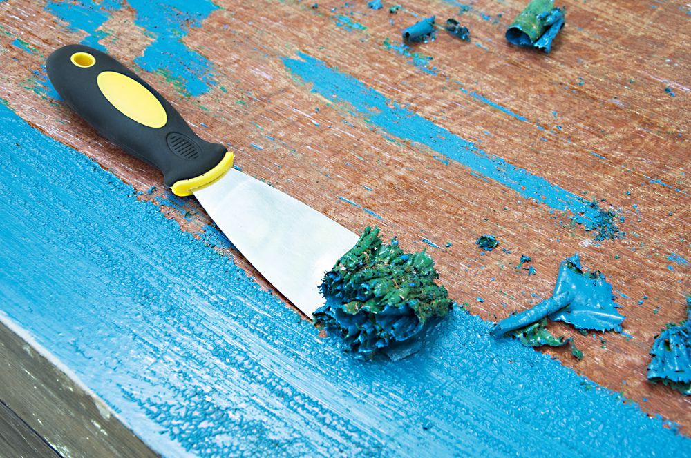 A spatula is being used to remove paint from a wooden surface.