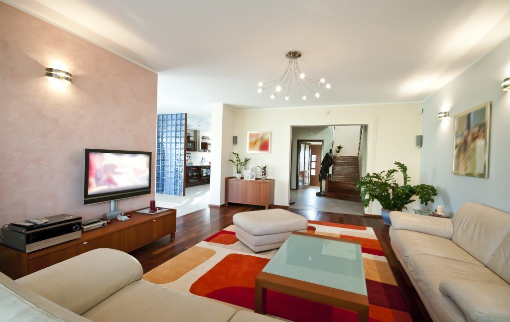 Spacious living room with white couches, a colorful rug, and a TV on a wooden console.