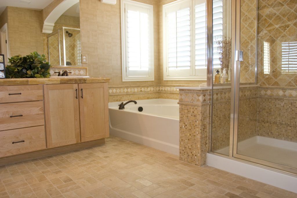Spacious bathroom with beige tile, wood cabinetry, a tub, shower, and a window with shutters.