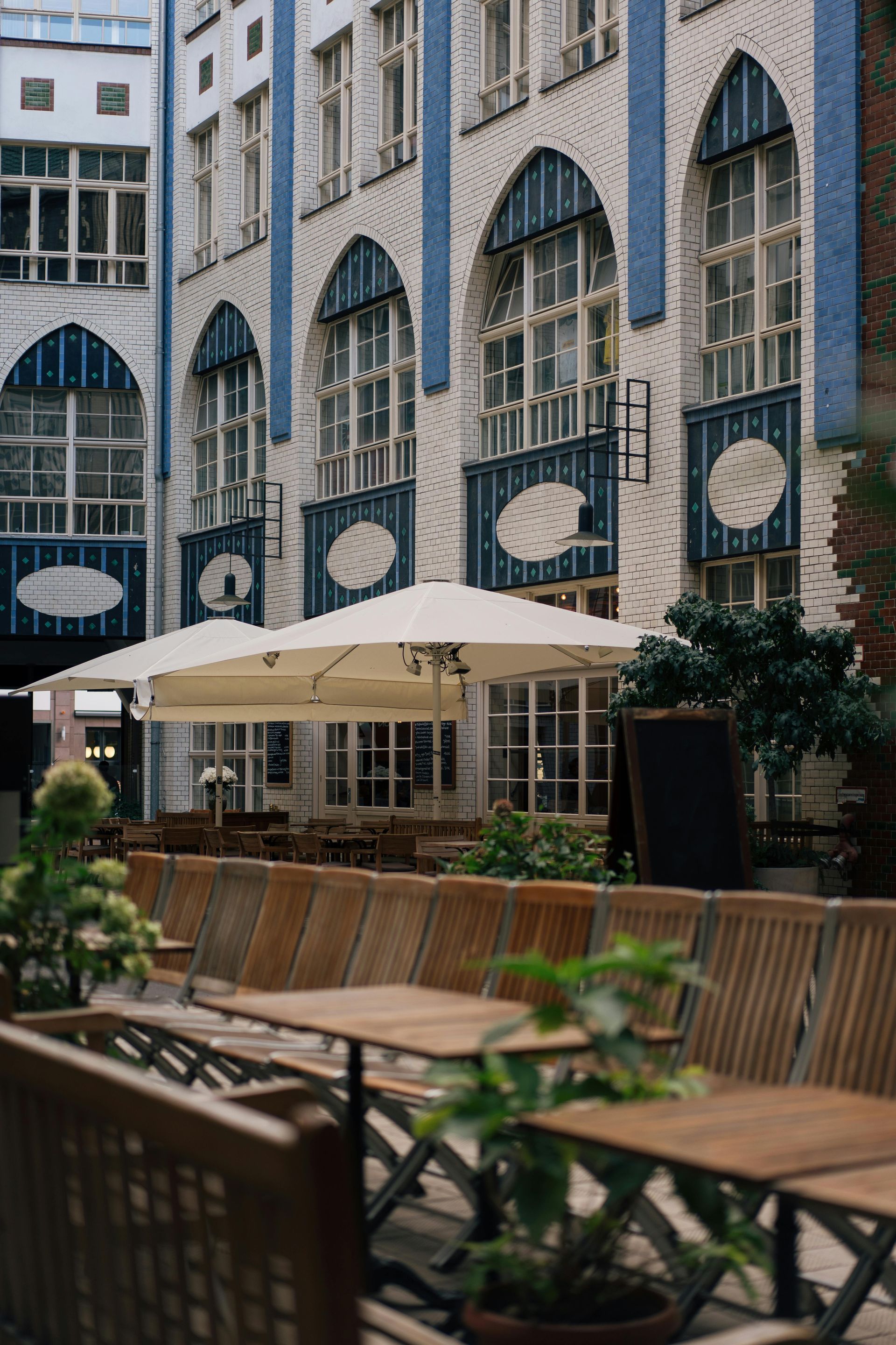 Outdoor cafe with wooden tables and umbrellas, set against a blue and white arched building.