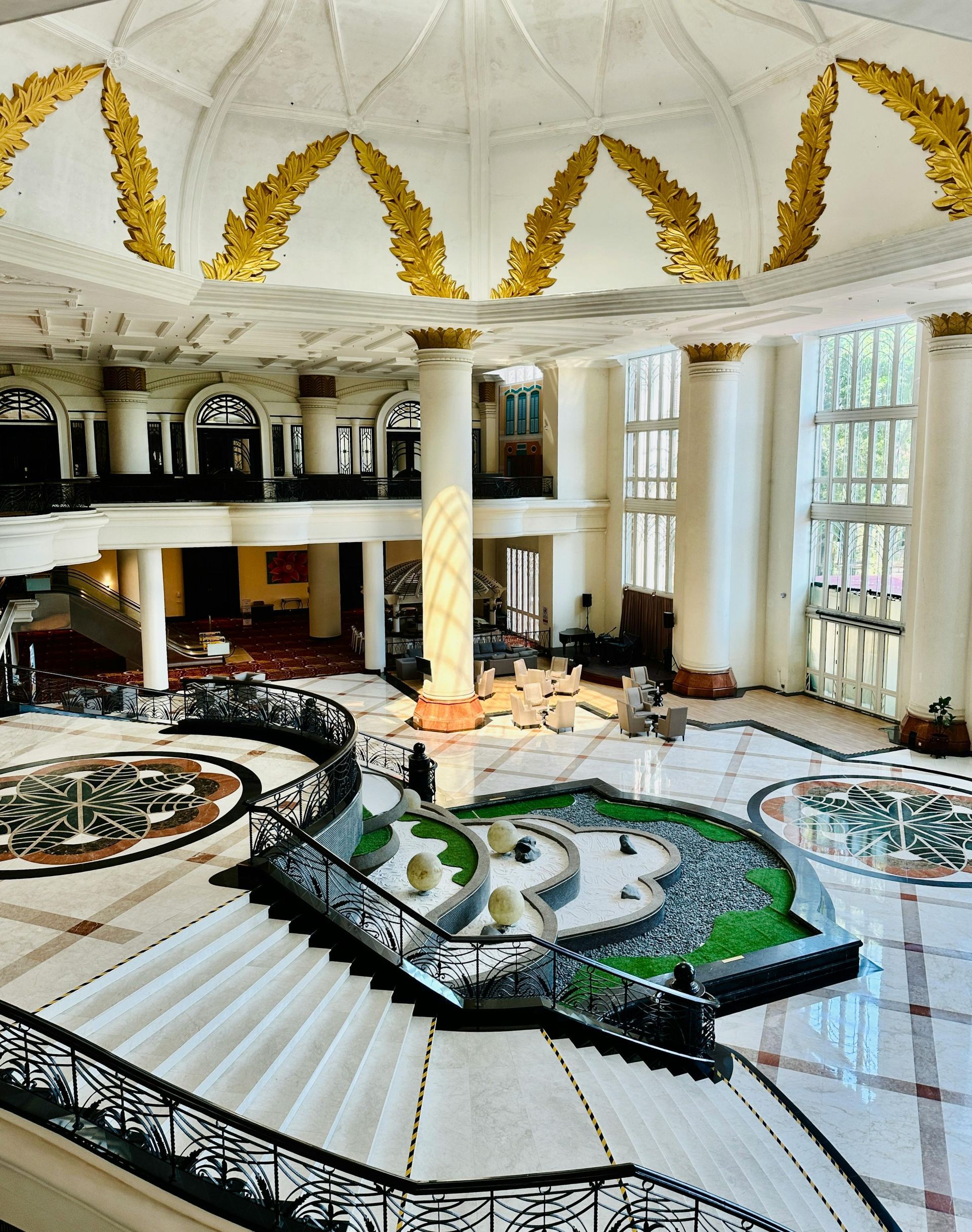 Ornate hotel lobby with a grand staircase and water feature. White and gold accents, natural light.