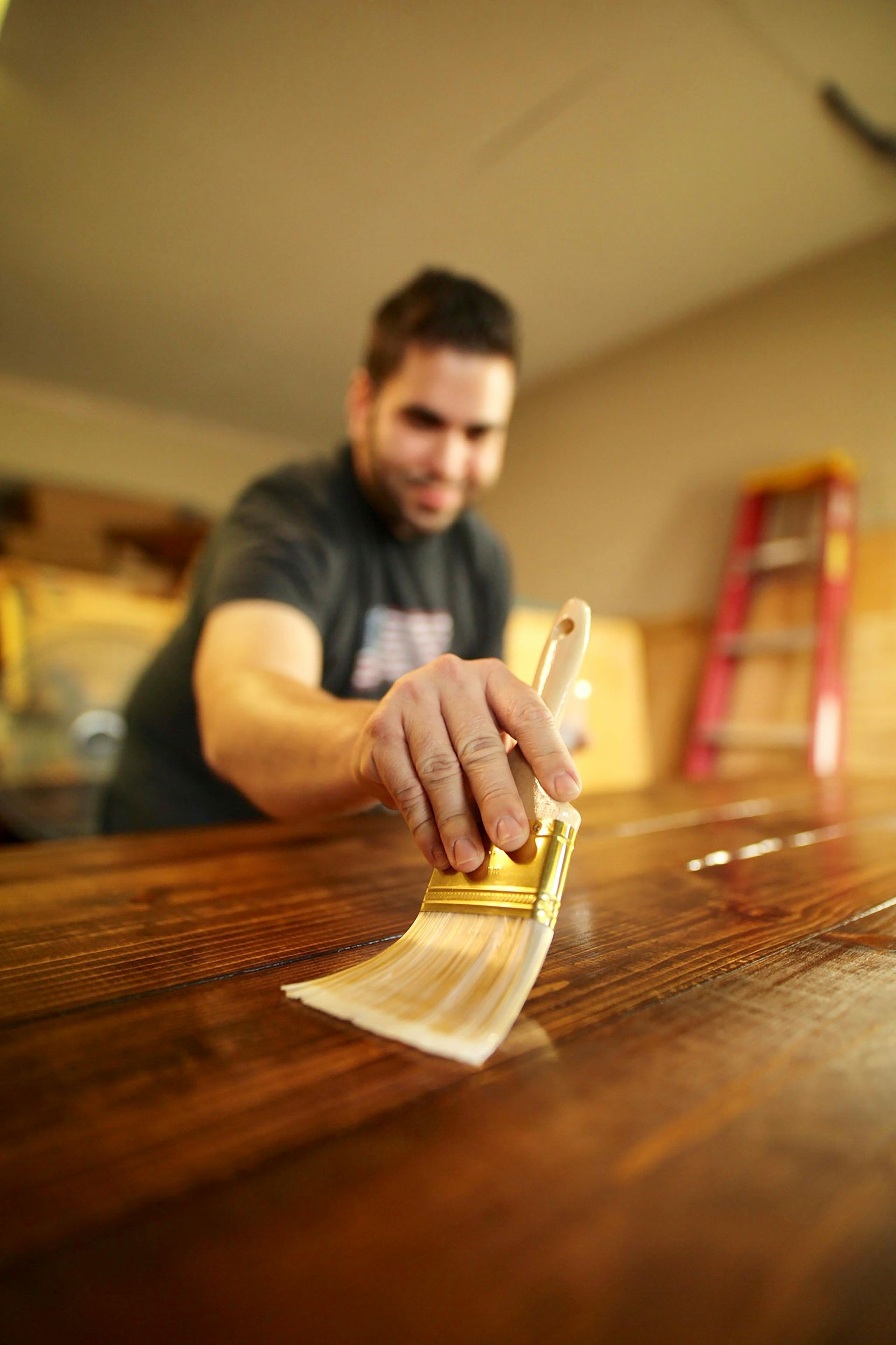 Man applying varnish to a wooden surface with a paintbrush.