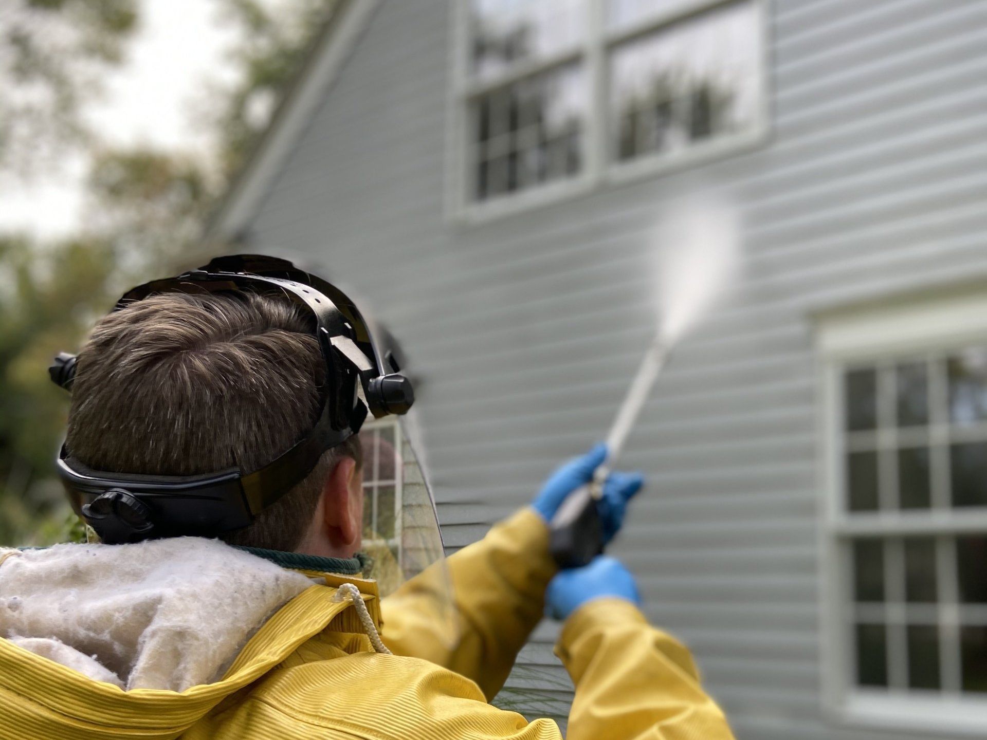 A man is cleaning the side of a house with a high pressure washer.