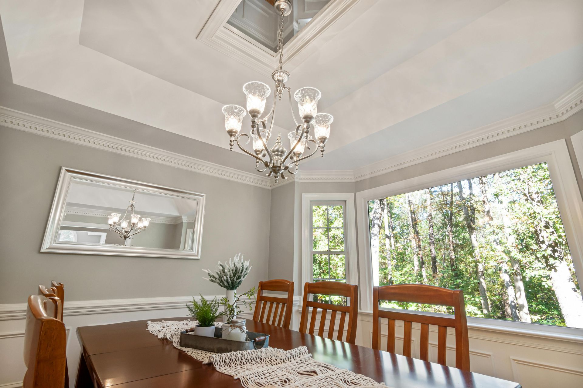 Dining room with chandelier, wood table, chairs, large window with trees.