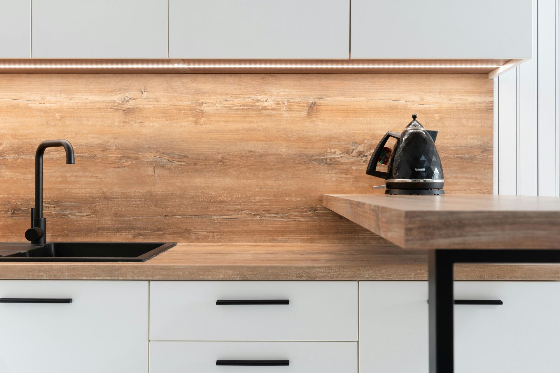 Modern kitchen with a black sink, faucet, and kettle; wood backsplash and countertops.