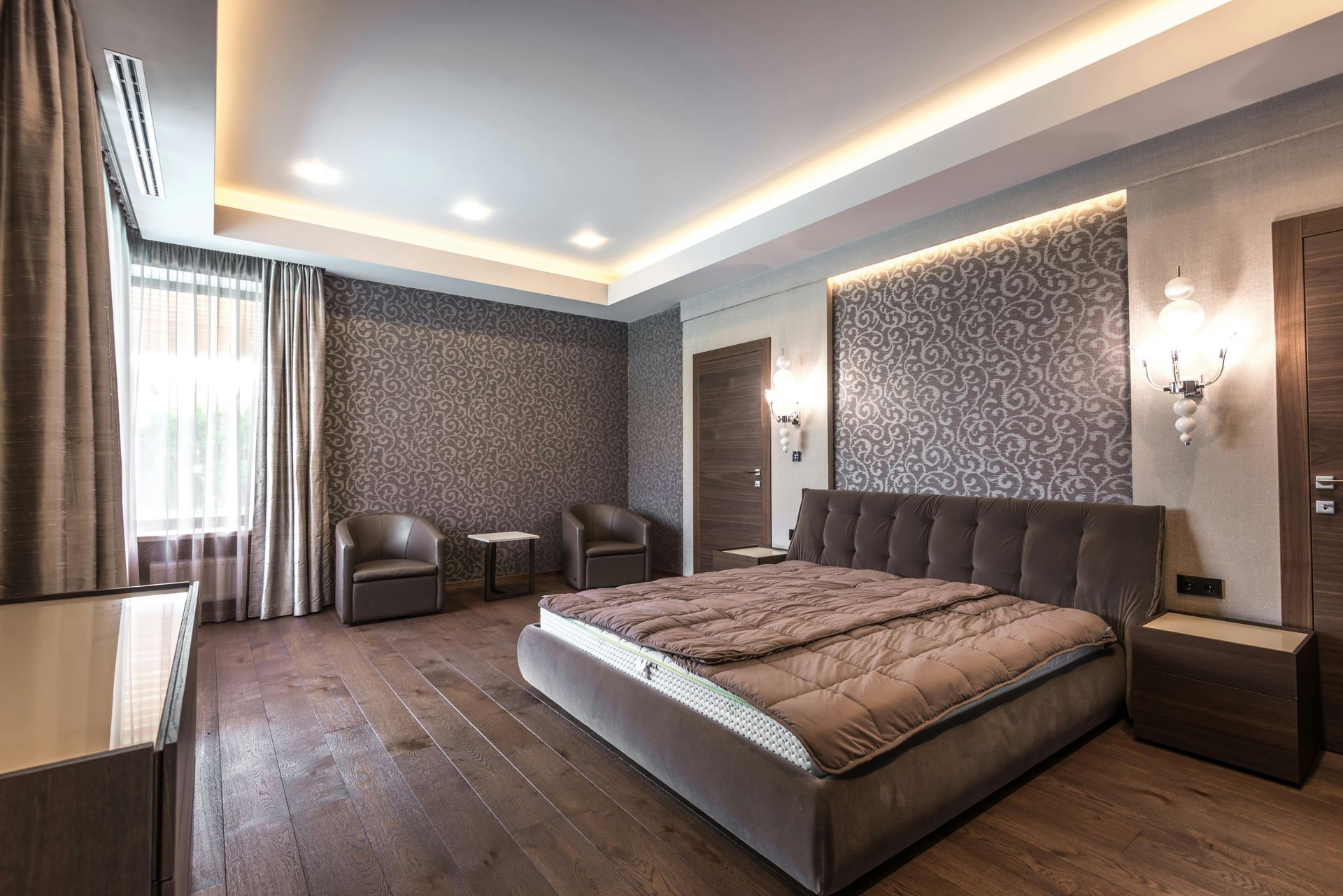 Bedroom with bed, armchairs, hardwood floor, wallpaper, and decorative lighting.