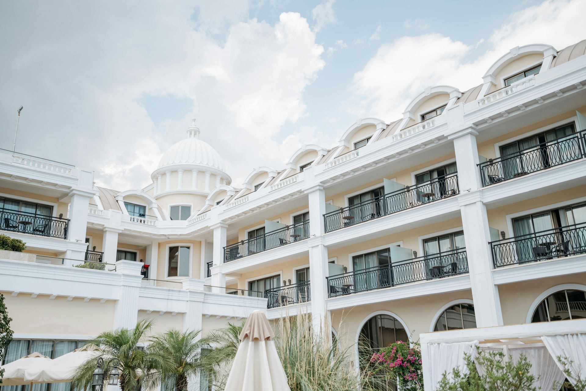 White hotel with dome and balconies under a cloudy sky.