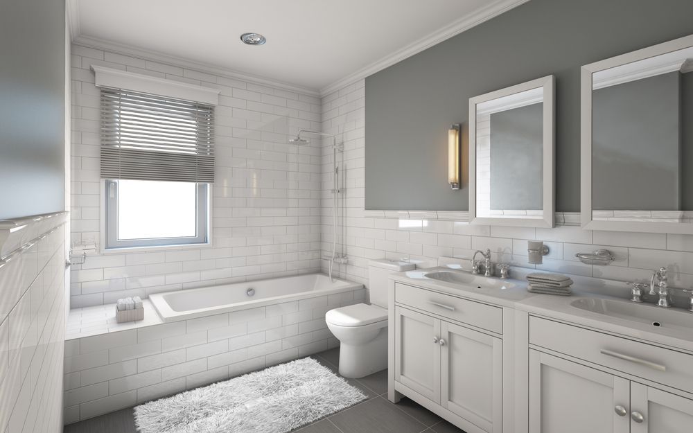 Bright white bathroom with a tub, toilet, double vanity, and a window with blinds.