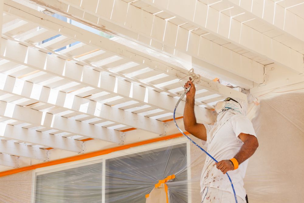 A man is spray painting the ceiling of a building.
