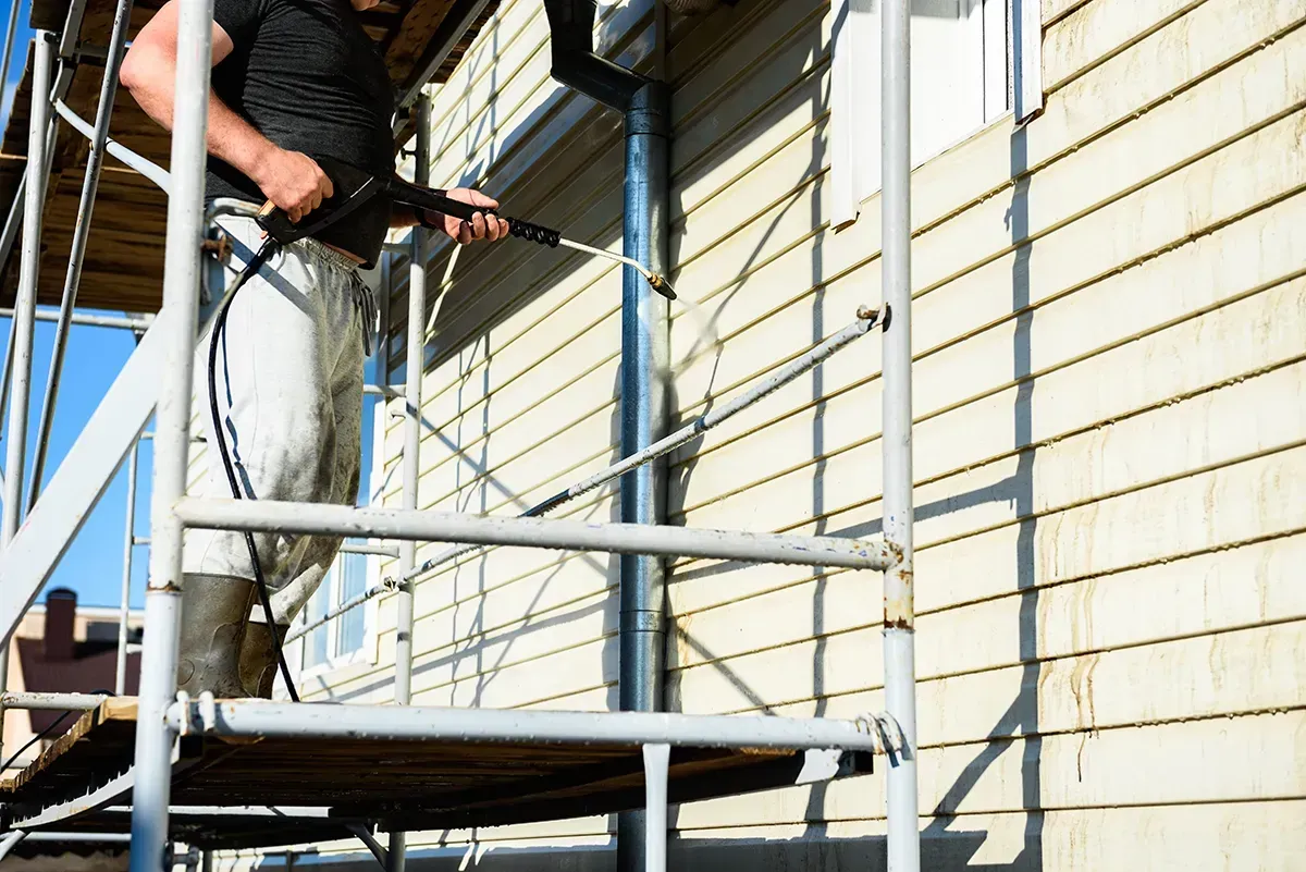 Worker power-washing a house wall from scaffolding